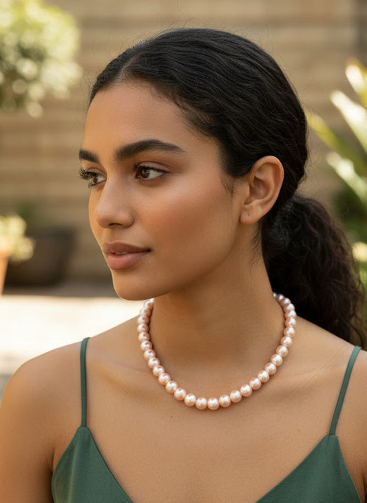 Woman wearing a pearl necklace outdoors with plants in the background